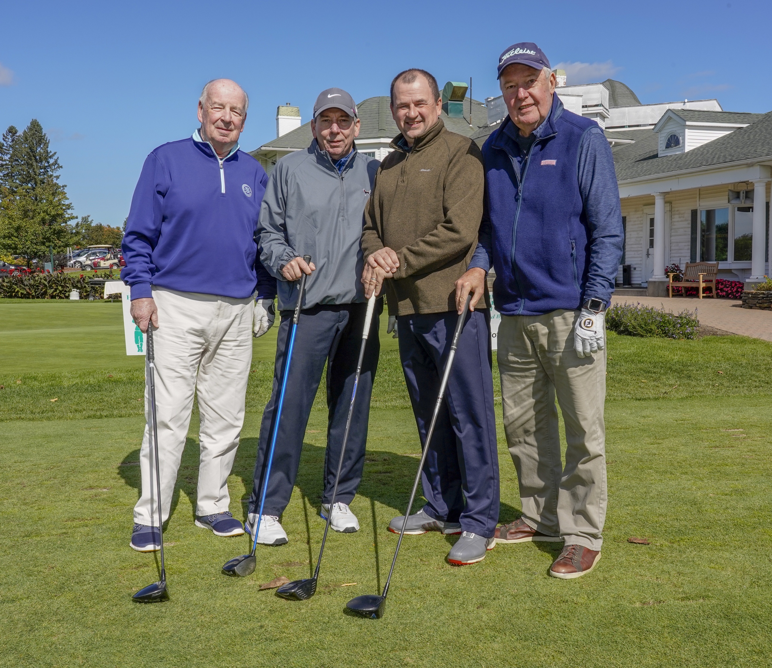 Four men stand with golf clubs